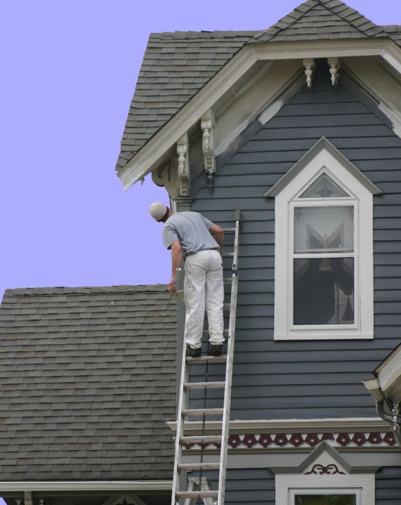 Painter from Victory Paints & Services Inc. working on the exterior of a traditional house in Riverside, CA, painting trim details on a sunny day.