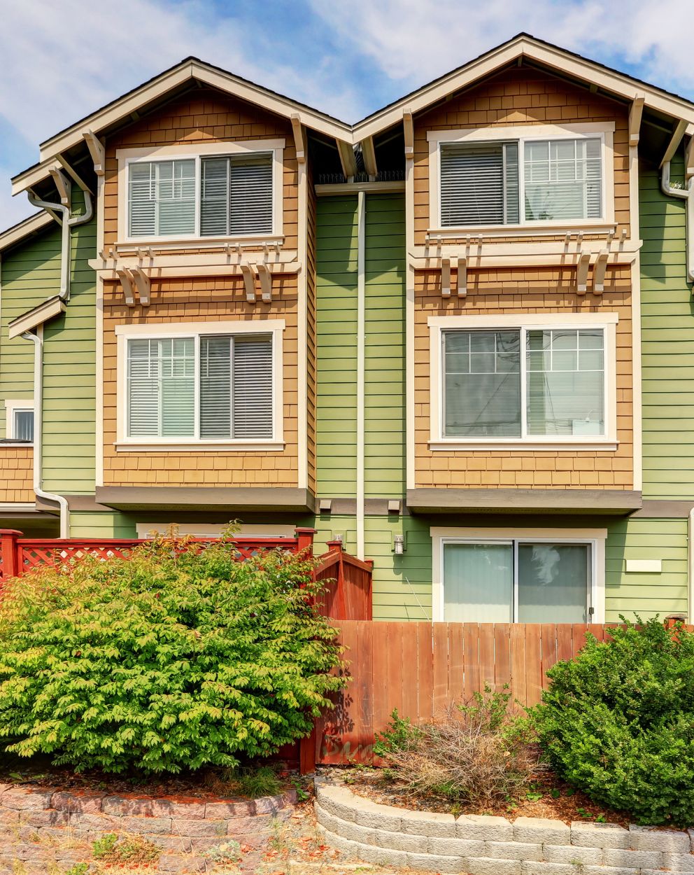 A freshly painted green and beige multi-story home surrounded by neatly maintained bushes and a wooden fence, showcasing professional interior and exterior painting services in Orangecrest, CA.